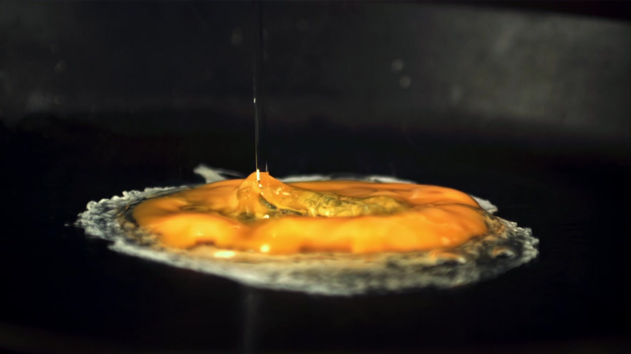 Slow Motion of Egg Yolk Frying on Hot Pan with Oil Pouring
