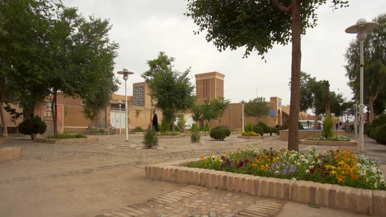 Static shot muslim woman walking crossing a dusty square in old city of Yazd, Southern Iran. Yazd is famous for it's wind towers or wind catchers and zoroastrian tradition.