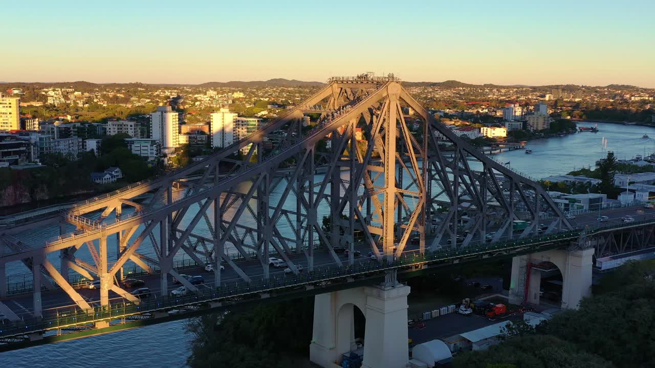 Cinematic aerial drone flyover Brisbane River capturing traffic crossing the iconic Story Bridge at sunset, with adventure climbers climbing on top of the bridge tower.