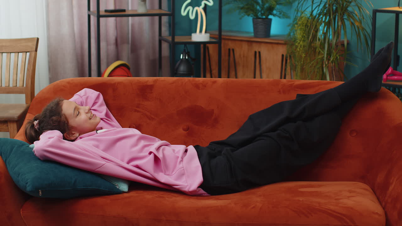 Tired happy preteen school girl lying down on orange couch taking a rest break enjoy daytime nap