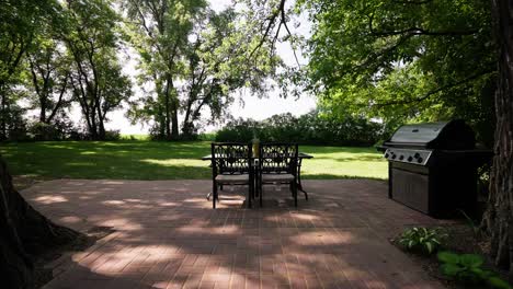 wide push in shot of an outdoor patio dinner table next to a grill in the backyard of a home on a sunny day