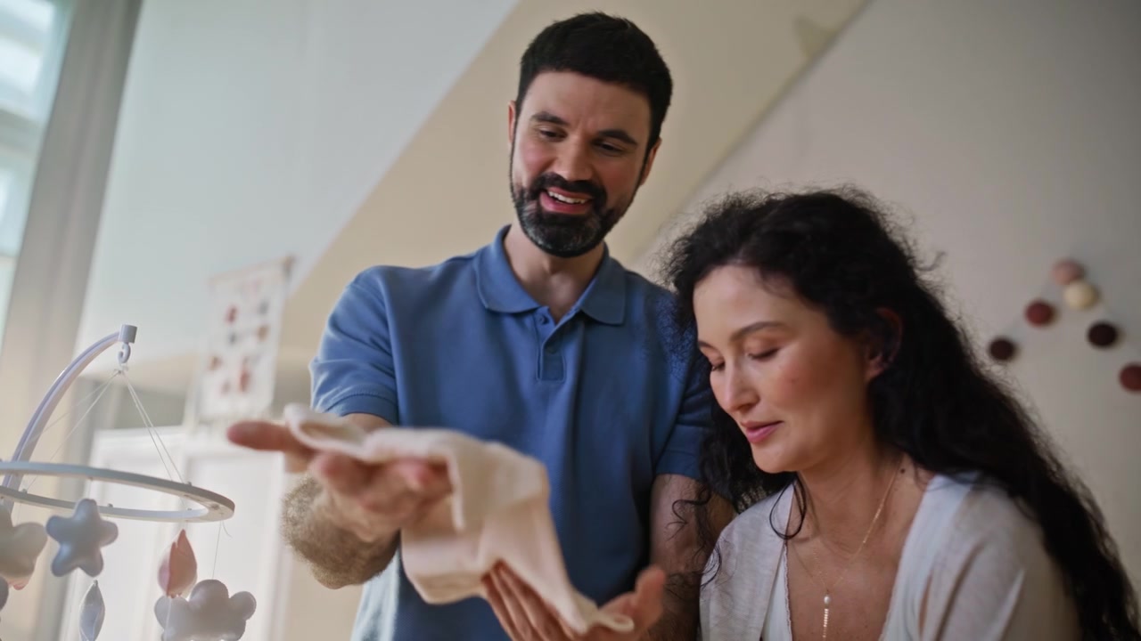 Futuros pais escolhendo roupas de bebê no quarto do bebê. Mulher grávida e marido perto do berço