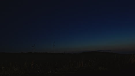 wind turbines at the horizon, almost dark blue night sky with car passing by