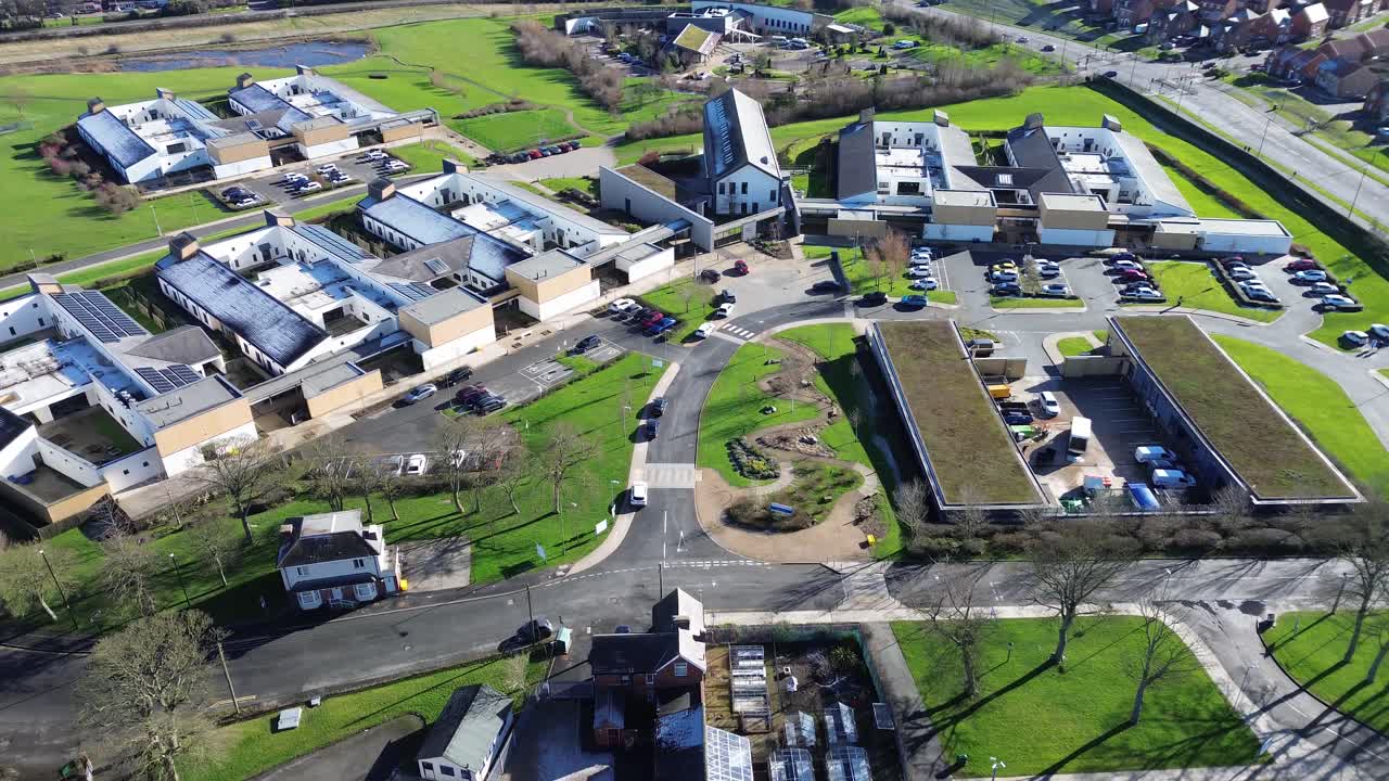 Hopewood psykiatrisk hospital: luftdrone panorering mod højre over NHS' psykiatriske campus i Tyne and Wear, England. Moderne hospitalsbygninger, veje, parkeringspladser, grønne områder på en solrig dag.