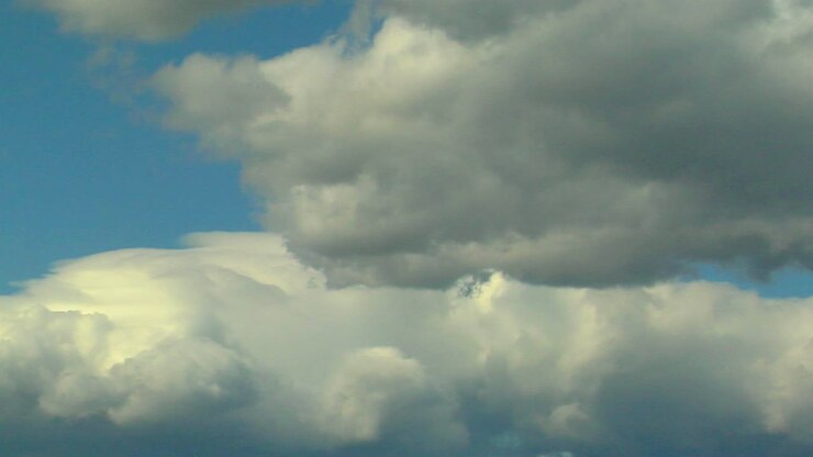 Billowy white clouds with gray undertones pass against a blue sky