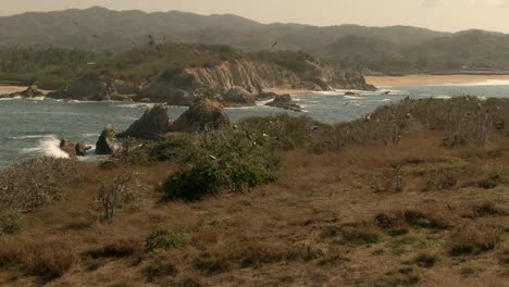 Flock-Of-Seabirds-Flying-Over-The-Rocky-Island-Near-El-Faro-de-Bucerias-In-Michoacan,-Mexico