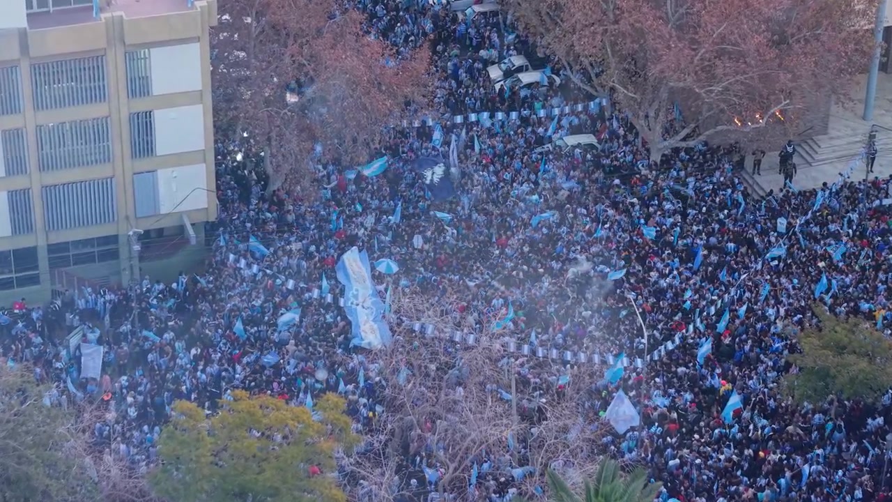 Folla entusiasta di tifosi di calcio argentini che saltano e sventolano bandiere nelle strade di San Juan. Zoom aereo in avanti in discesa nel pomeriggio