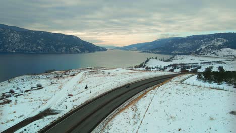 Magia-Invernal-En-El-Centro-De-Okanagan:-Una-Vista-Aérea-Del-Paisaje-Cubierto-De-Nieve,-El-Tráfico-En-La-Autopista-97-Y-El-Lago-De-Madera