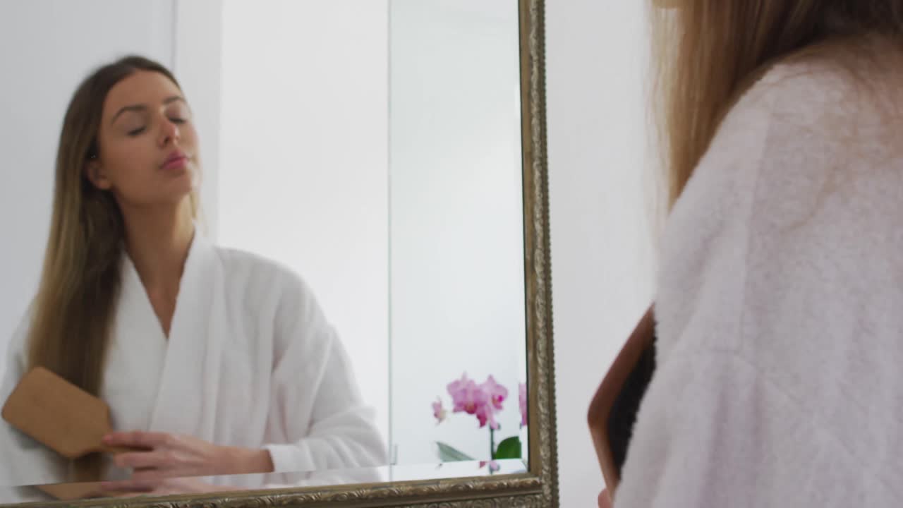 Donna in accappatoio che si spazzola i capelli mentre si guarda allo specchio