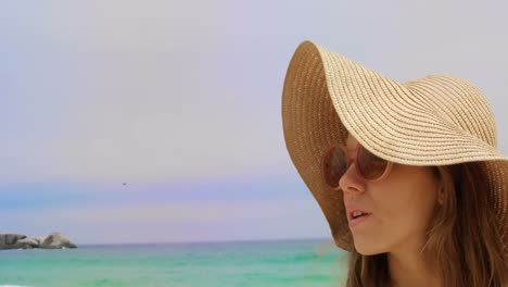 Vista-Frontal-De-Una-Mujer-Caucásica-Con-Sombrero-Y-Gafas-De-Sol-Parada-En-La-Playa-4k