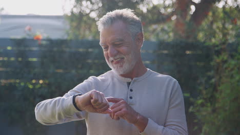 senior hispanic man checking smart watch in garden at home