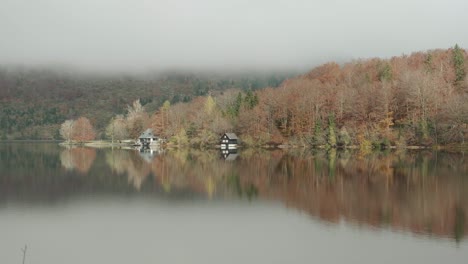 reflection of lake bohinj during the fall season with amazing orange autumn colours with a boat hut on the lake edge