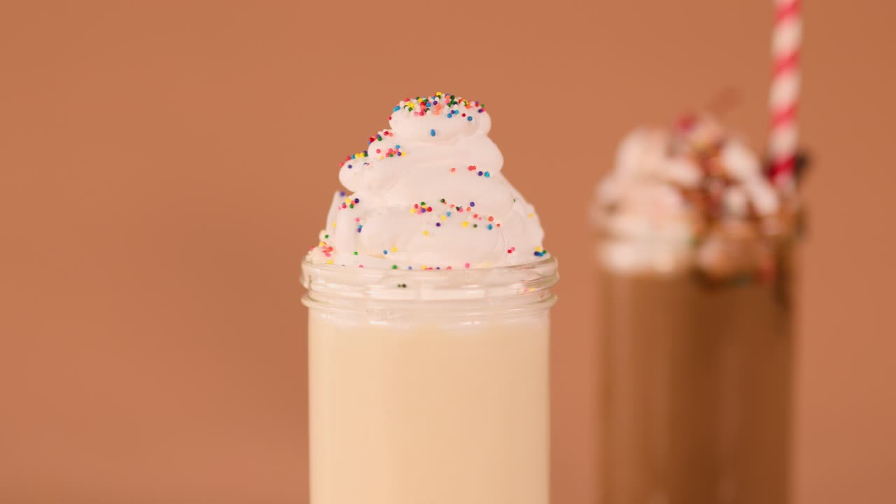 Close-up vanilla milkshake topped with whipped cream and cherry, warm studio lighting, static camera