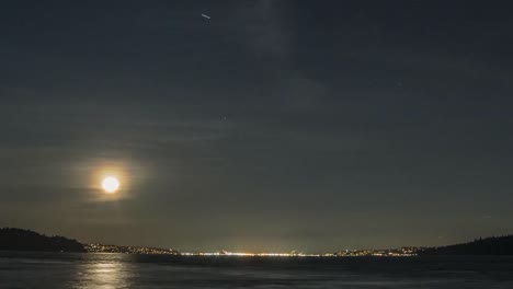 slow zoom in of full moon rising above dark shimmering water, tacoma washington, moving time lapse