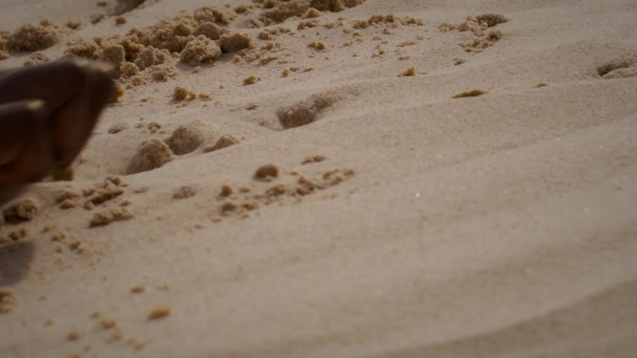 Primo piano di una mano aborigena australiana che traccia motivi nella sabbia soffice, simboleggiando la narrazione, la cultura e la connessione alla terra attraverso i segni tradizionali.