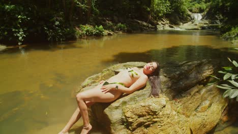 latina girl in a bikini body tape laying on a rock at a flowing waterfall in the caribbean island