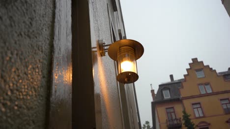 warm street lamp glowing on a rainy day, droplets on wall, overcast sky, european architecture in the background