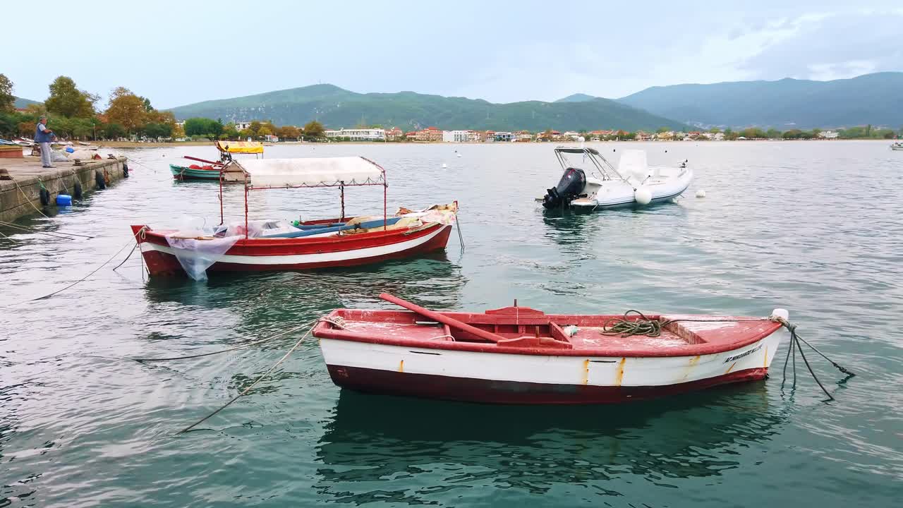 STAVROS, GREECE - SEPTEMBER 26, 2020: Moored boats on the shore of the Aegean sea, town and hills on the background, cloudy sky