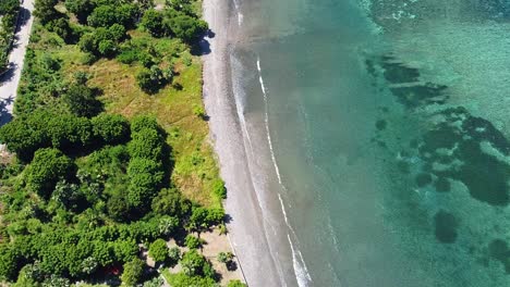 aerial view of remote tropical island with green trees, beach and gentle waves rolling in from crystal clear ocean water with coral reef