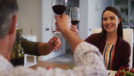 madre caucásica sonriente haciendo un brindis con el marido y el padre en la mesa antes de la comida familiar