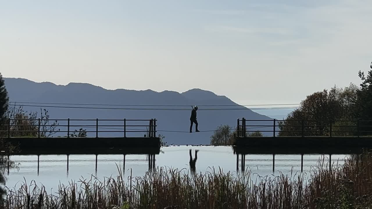인식할 수 없는 백라이트 사람이 밧줄 모험 공원의 티베트 다리에서 연못을 건너다