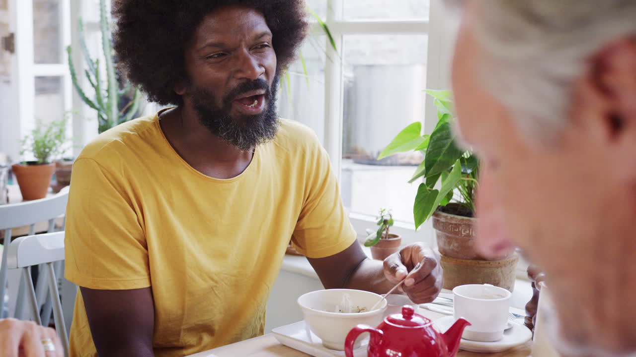 Middle aged black man eating breakfast with friends at a cafe, close up, selective focus