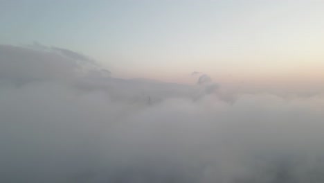 Aerial-close-up-shot-of-a-wind-turbine-generating-renewable-energy-from-the-wind-surrounded-with-white-clouds-in-Golan-Heights,-Israel-at-sunset