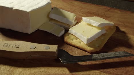 close up slices of brie cheese put onto soda cracker, knife on board