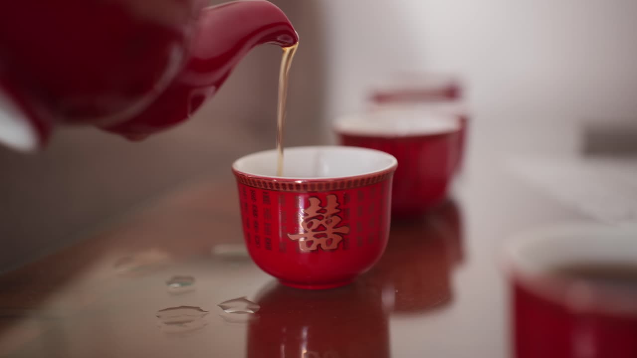 Servindo chá chinês tradicional de bule vermelho em xícaras em câmera lenta