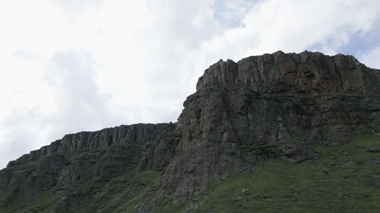 vuelo aéreo hacia escarpados acantilados rocosos fuera de la meseta verde de la montaña.
