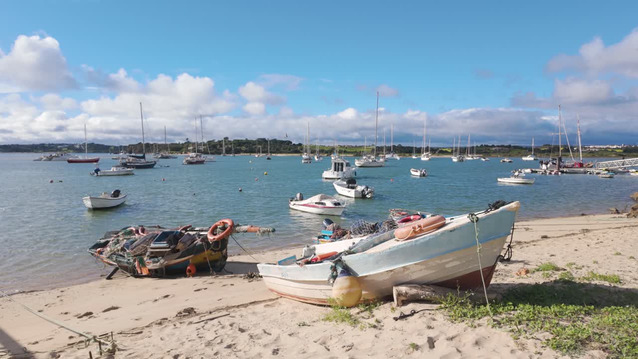 A scenic view of Alvor, Portugal, showing boats anchored and beached on sand in the harbor with the town in the background