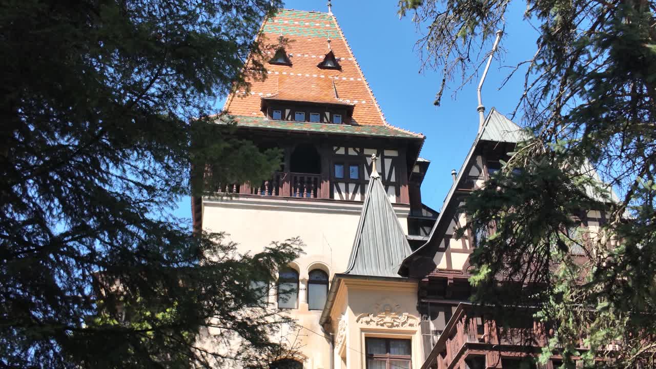 Smooth tilt-up shot revealing Pelișor Castle as it rises behind tree branches in Sinaia, Romania