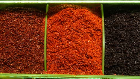 close up of red pepper flakes, black pepper, and ground pepper in a spice rack