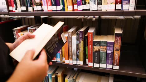 person choosing a book from library shelf