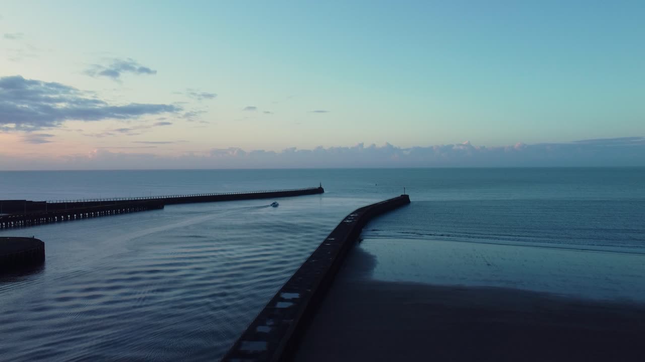 Ripresa aerea ascendente di una piccola barca che lascia la Marina di Swansea con un molo su ogni lato e un'alba dorata su un oceano calmo. Mare aperto con l'avventura che attende
