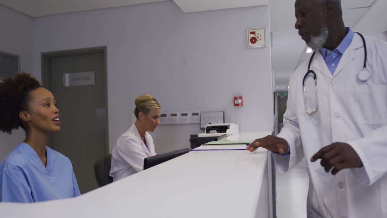 Médico de diversas etnias chegando à recepção do hospital e conversando com uma funcionária.