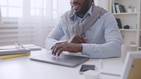 hombre afroamericano terminando el trabajo en la computadora portátil, sentado en la acogedora oficina de casa