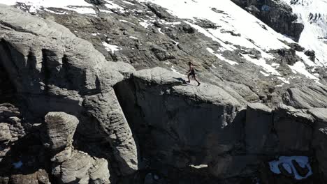 man is walking confidently upwards on an angled cliff on the side of a mountain with bare rocks and snow