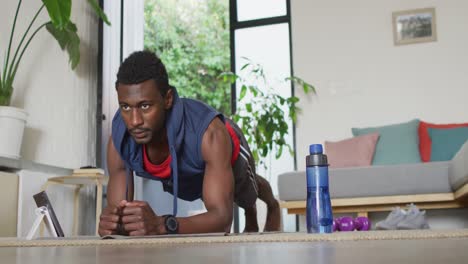 happy african american man exercising in living room, using tablet