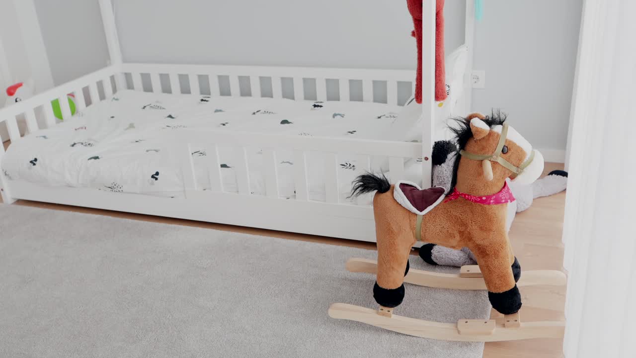 Rocking horse toy next to toddler bed in cozy light filled children’s room