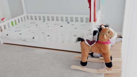 rocking horse toy next to toddler bed in cozy light filled children’s room