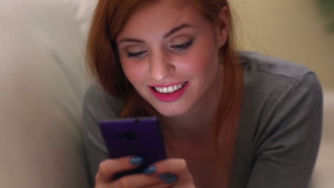 hermosa morena acostada en el sofá usando un teléfono inteligente