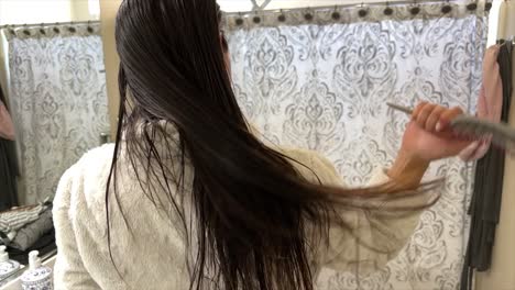 Woman-Brushing-Wet-Hair-In-Bathroom-Viewed-From-Behind