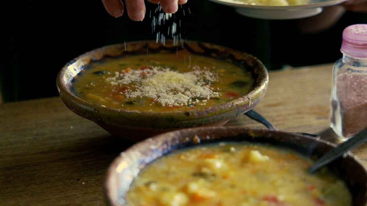 Mano Espolvoreando Queso Rallado en un Tazón de Sopa de Verduras
