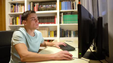 a man working on a computer at a desk with a bookshelf in the background