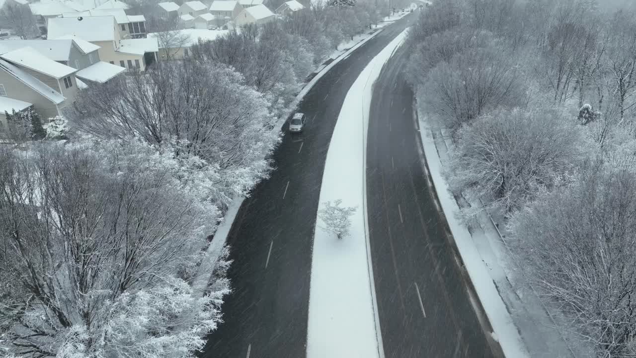 Quiet suburban winter morning in United States, snowy homes and frosted trees lining calm street, soft dawn light revealing fresh tire tracks through snow. Peaceful cold season in USA. Aerial view