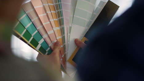 woman hands touching swatches book indoors. unknown couple using color palette.