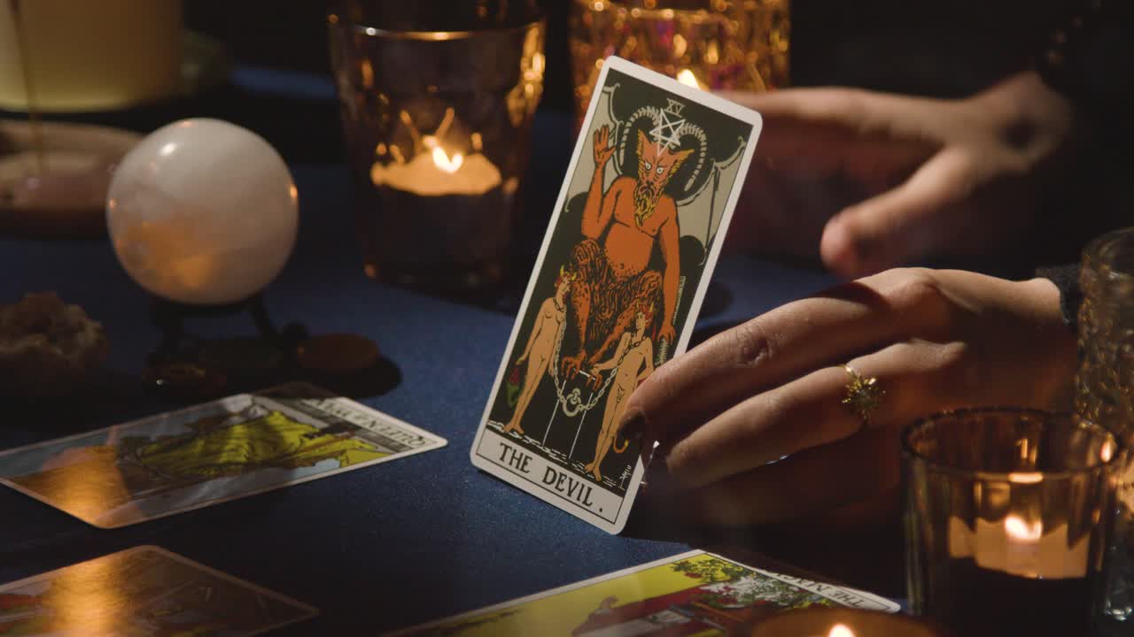 primer plano de una mujer dando una lectura de cartas del tarot en una mesa a la luz de las velas sosteniendo la carta del diablo 1