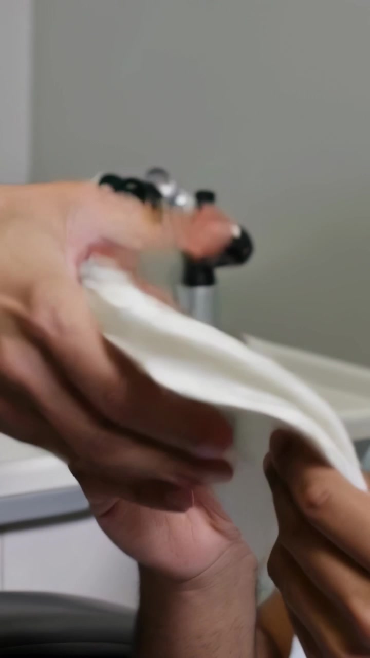 Video verticale: Medico in camice bianco che prende una garza e la porge al paziente in camicia blu, pulendogli il collo per l'esame.