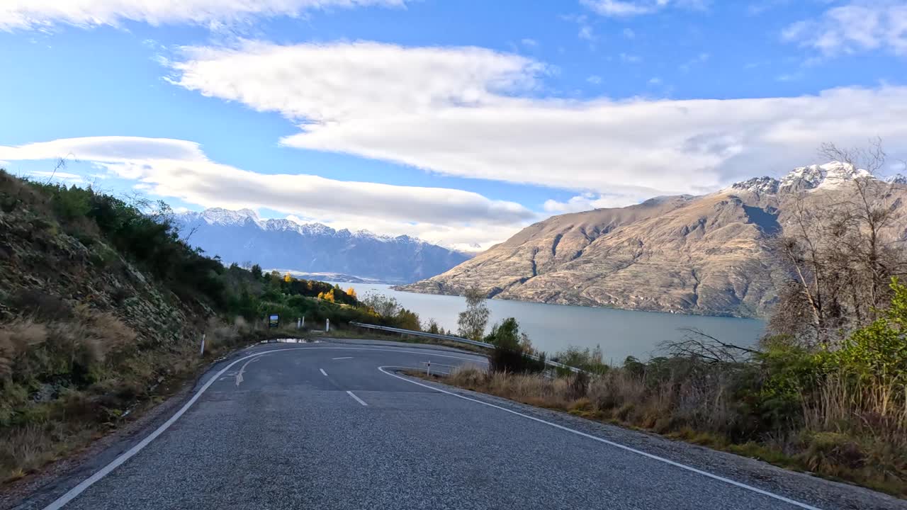 Timelapse car journey through forested mountain road, revealing lake and snow-capped peaks, daylight